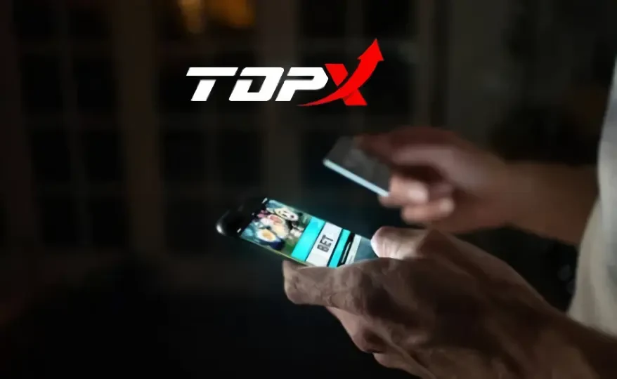 Mãos segurando um celular com um jogo de cassino na tela, com o logotipo da TopX